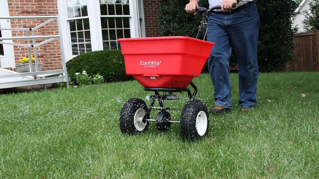 Earthway broadcast fertilizer spreader being pushed across a green lawn.