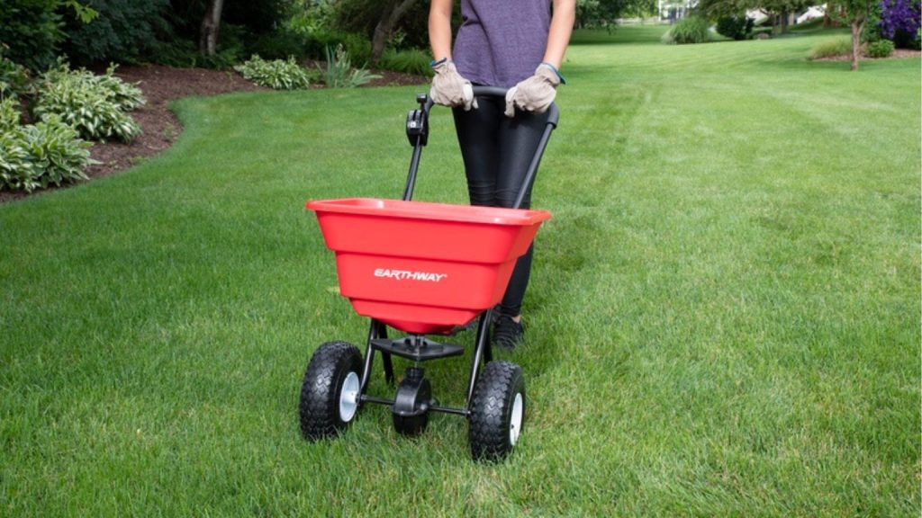 A broadcast rotary spreader being pushed across a green lawn in early spring in a Southwest Ohio residential yard.